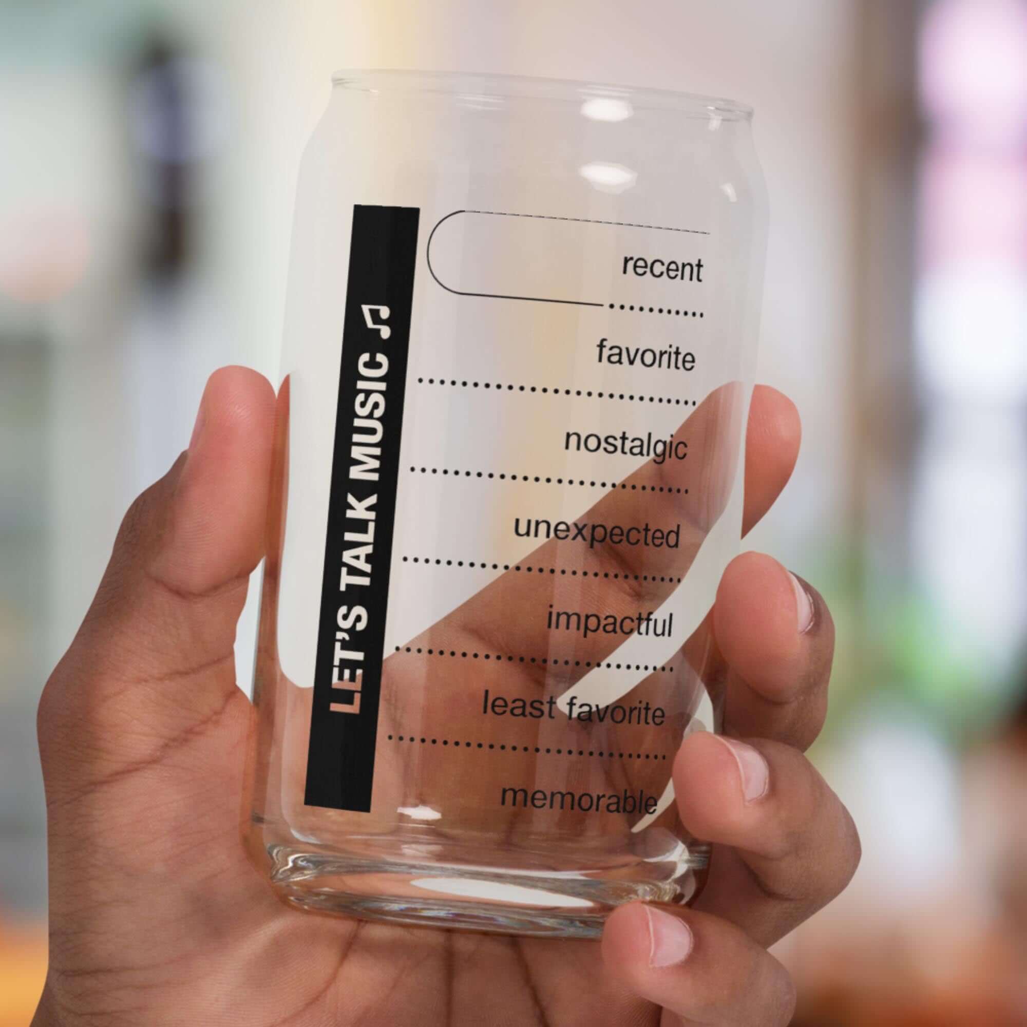Hand holding a Conversation Starter glass with prompts for music memories and stories, perfect for gatherings.